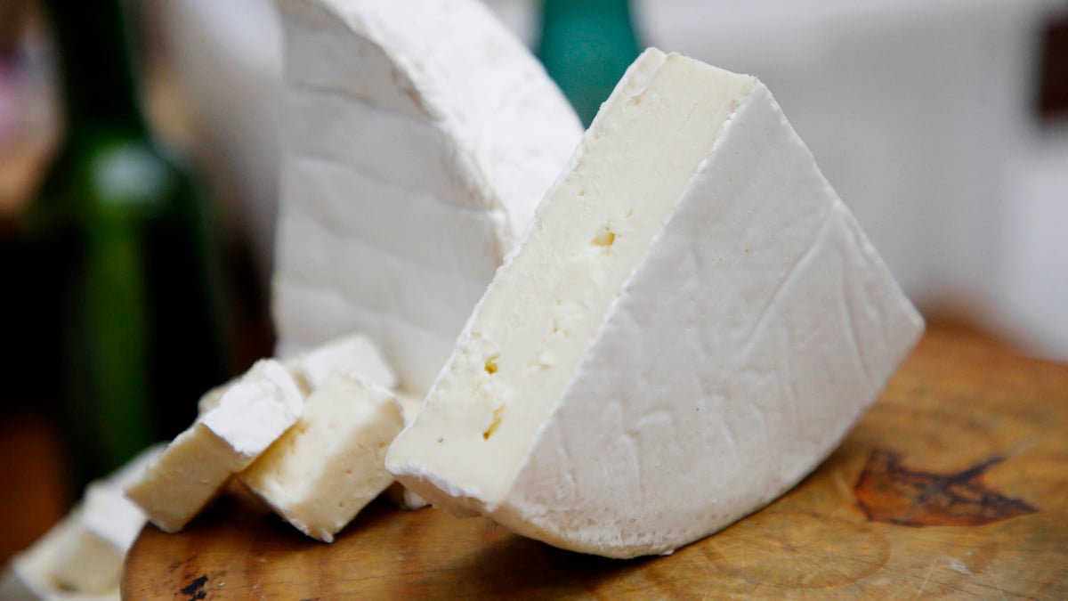 Queijos artesanais de casca branca cortados em fatias sobre tábua de madeira