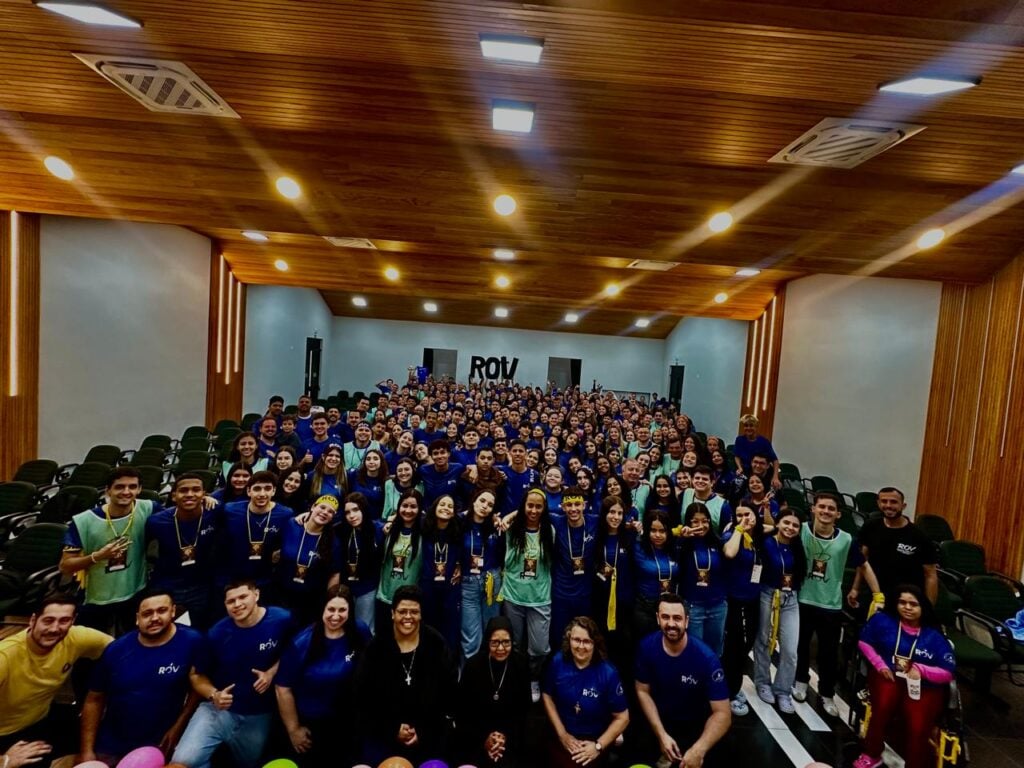 Jovens participantes do Retiro de Orientação Vocacional reunidos em auditório com o logotipo ROV ao fundo