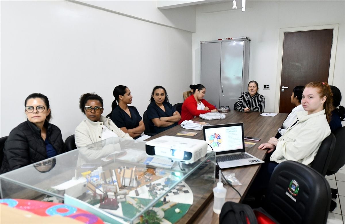 Pessoas sentadas ao redor de mesa de reunião com notebook e projetor